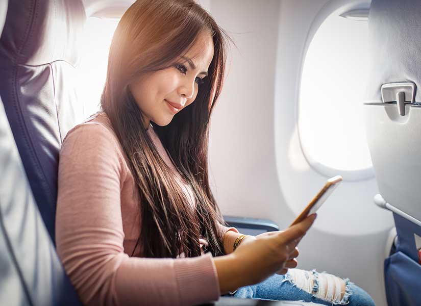 Woman sitting on airplane using a mobile phone - in-flight connectivity