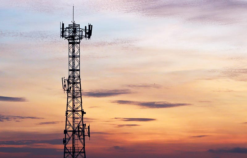 cell tower in foreground with orange sky in background from setting sun