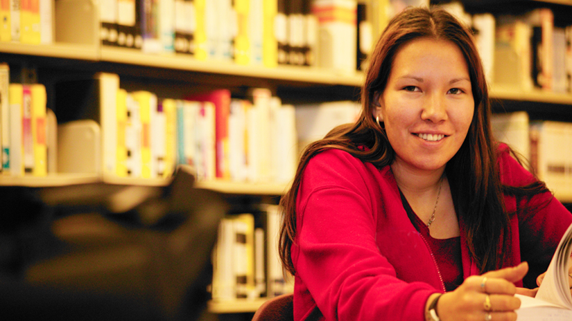 Young female student sitting in library with shelves of books in the background