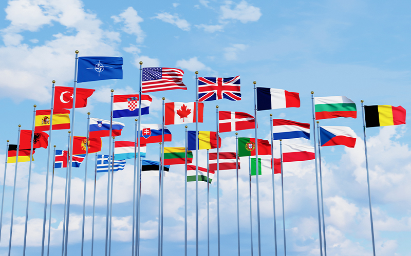 A vibrant row of national flags from various countries fluttering in the wind against a clear blue sky, symbolizing international unity and diversity.