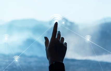 Hand reaching toward wireless connectivity icons over a remote mountain landscape, illustrating rural broadband access and network infrastructure in underserved areas